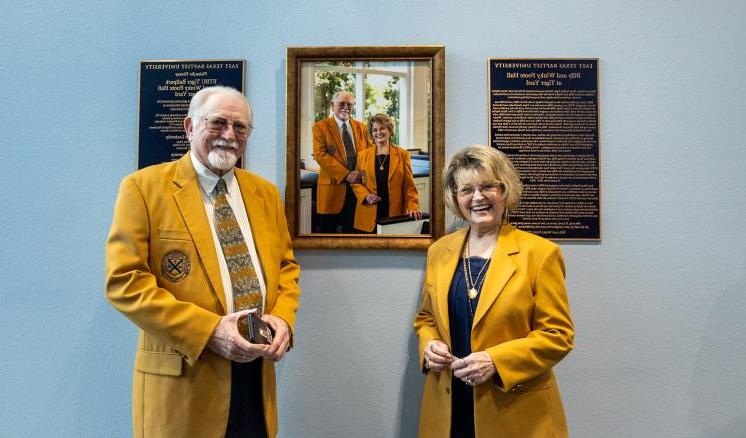 身穿金色夹克的男女站在墙上的肖像前对着镜头微笑.